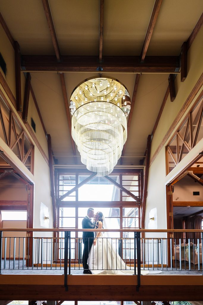Bride and groom embrace on the railing landing beneath the cascading crystal chandelier