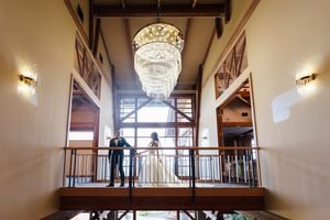 The couple stands hand in hand on the timber landing with the chandelier glowing above them