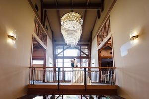 Bride and groom hold each other on the timber mezzanine landing underneath a chandelier