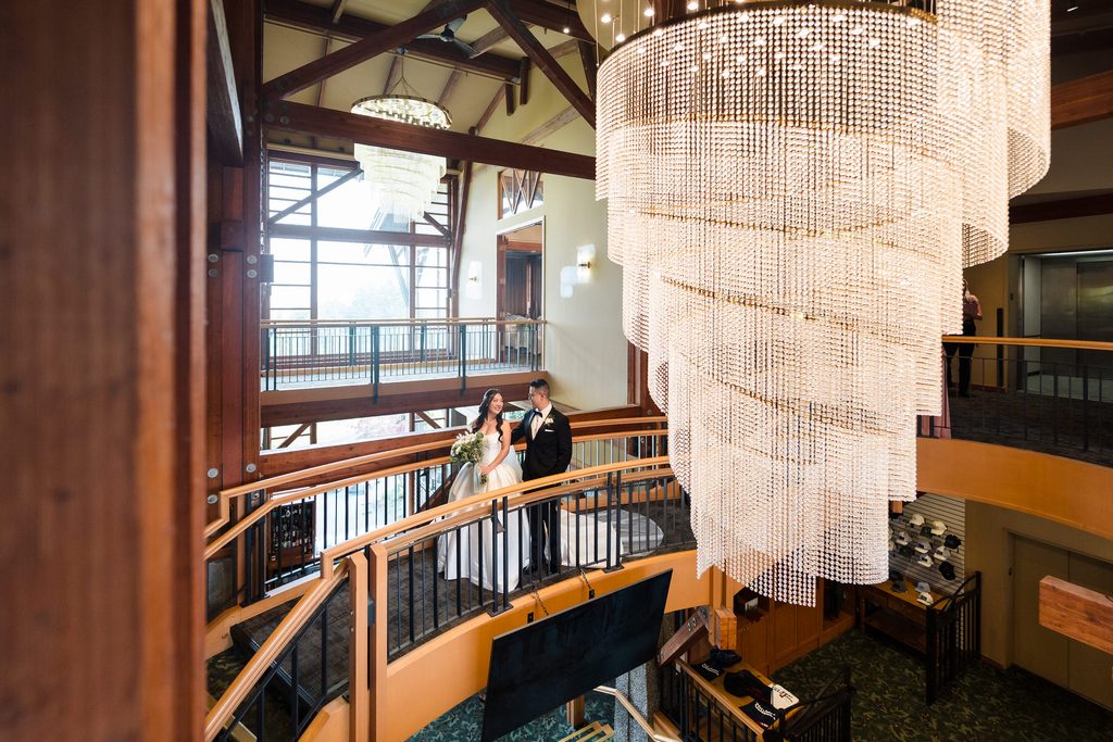 The bride's bouquet catches the light as the couple stands on the curved staircase underneath a chandelier