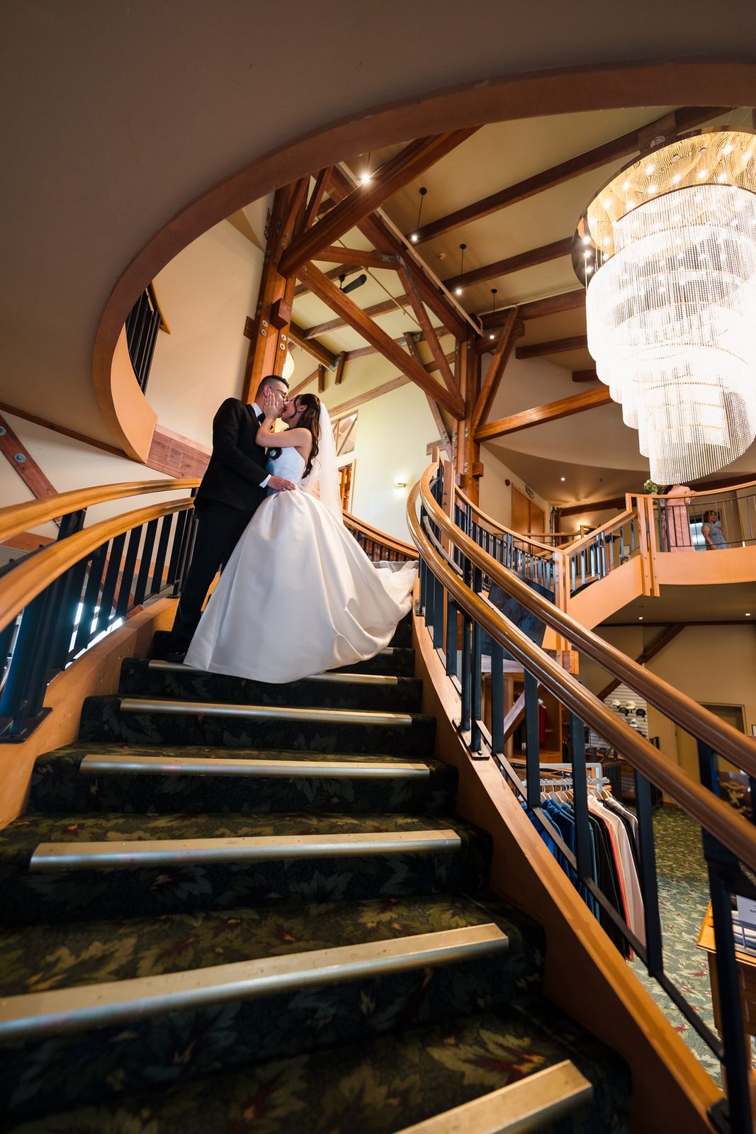 Couple kissing on the curved staircase with a chandelier in the background with high ceilings.