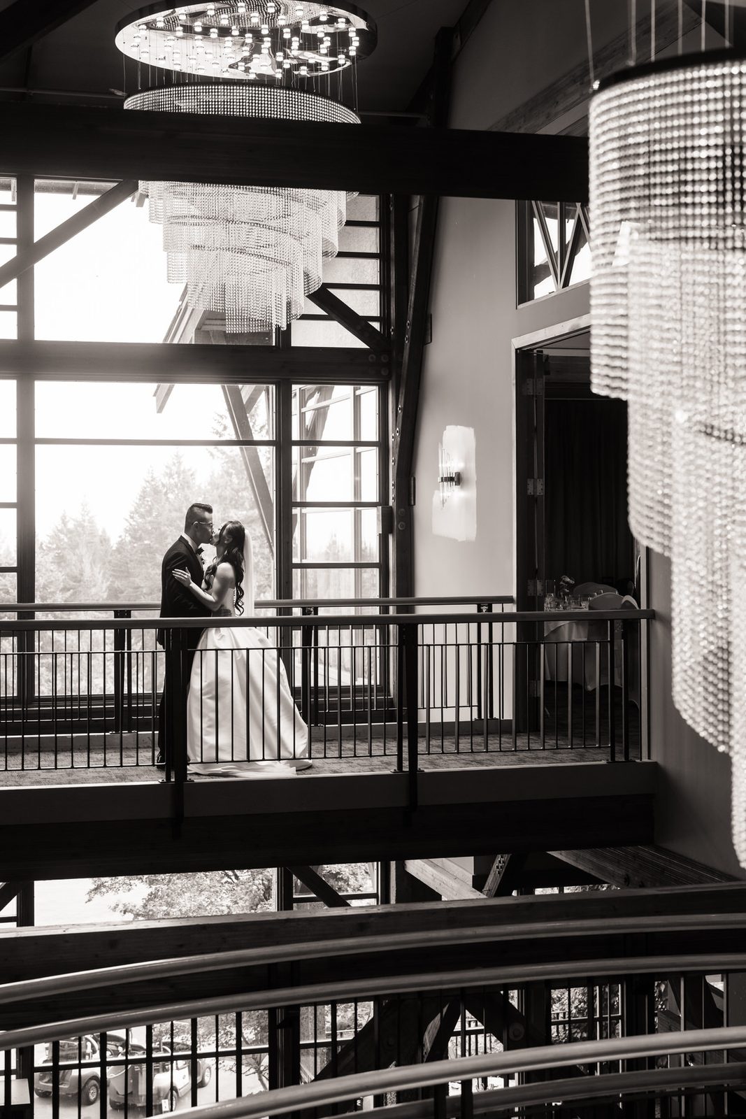 Kissing underneath the chandelier in front of a large bay window surrounded by chandeliers.