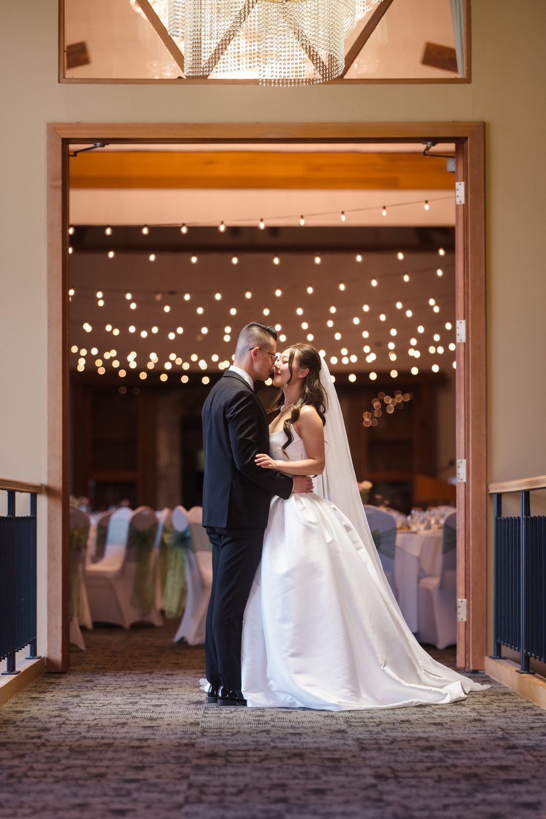 The couple kisses beneath the string lights strung across the ballroom entrance