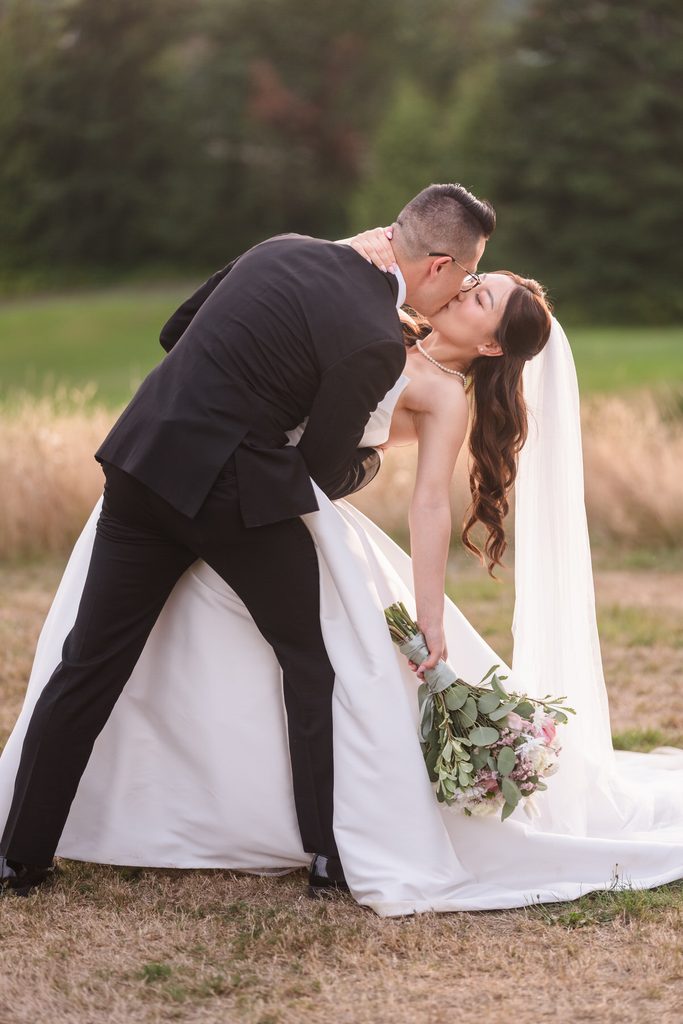The groom dips the bride for a kiss as golden hour light catches her veil.