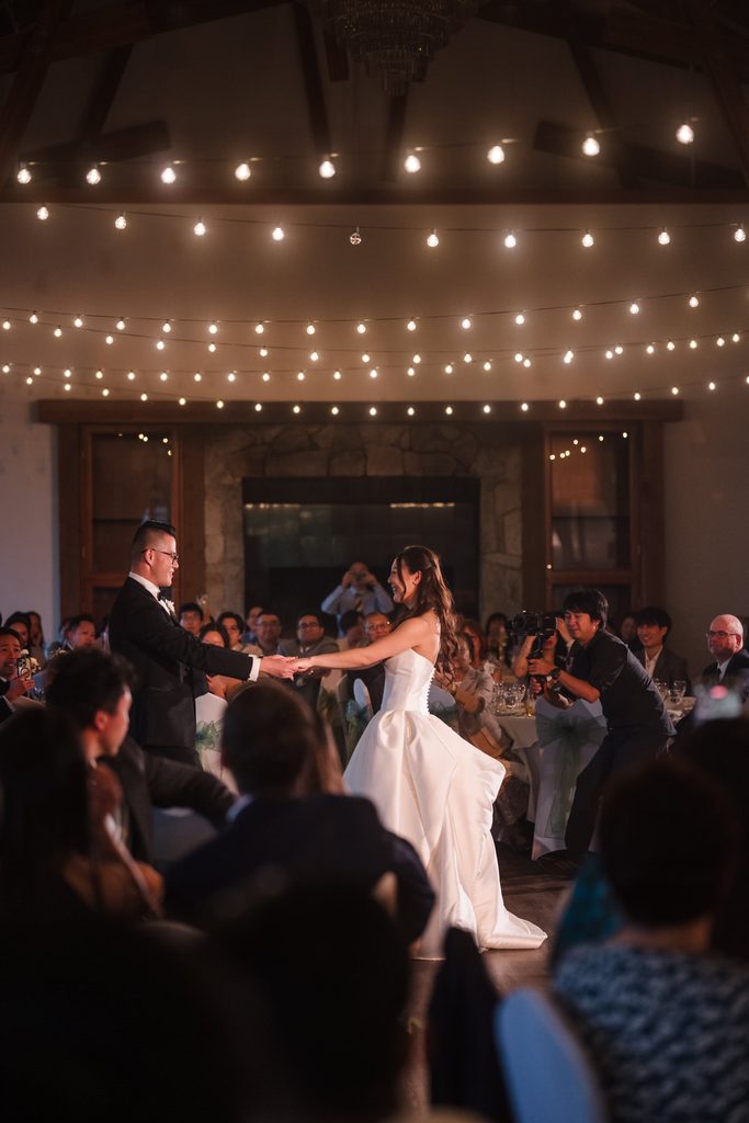 The groom pulls the bride into a close embrace under the timber hall's string lights.