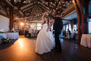 Warm light glows behind the couple as they are doing the first dance, surrounded by their wedding guest underneath string lights.