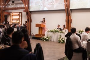 A bridesmaid making a toast to the bride and groom with their guests in the background underneath the string lights.