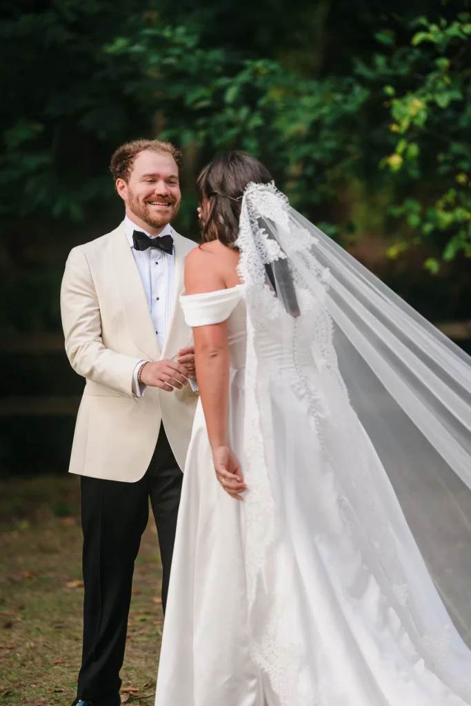 Groom smiling warmly as he faces the bride, her lace edged veil in the foreground