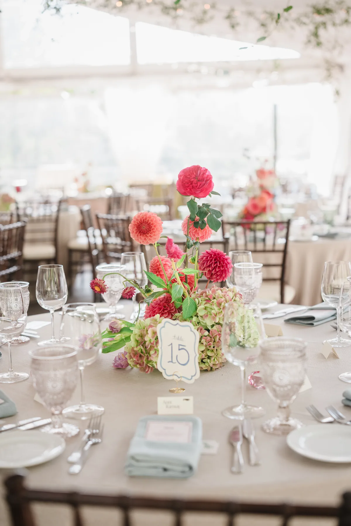 Long reception table with pink dahlia florals, glassware and folded sage napkins