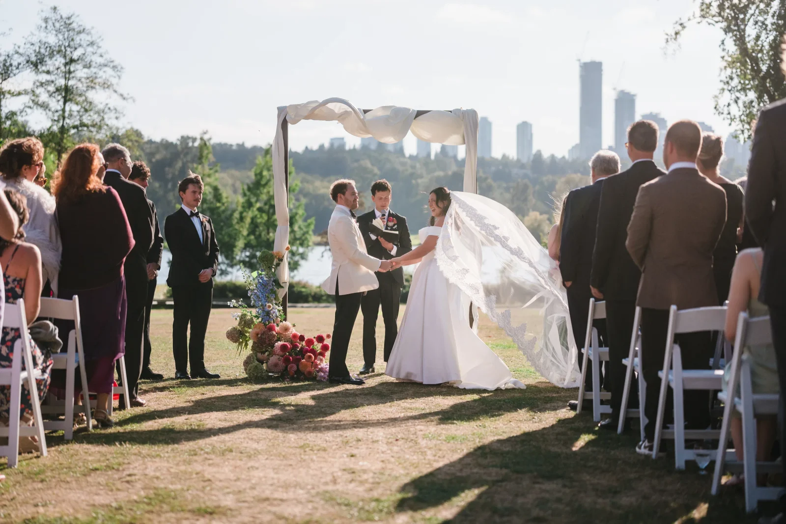 Groom holds the bride's hands while a man in a black suit reads into a mic