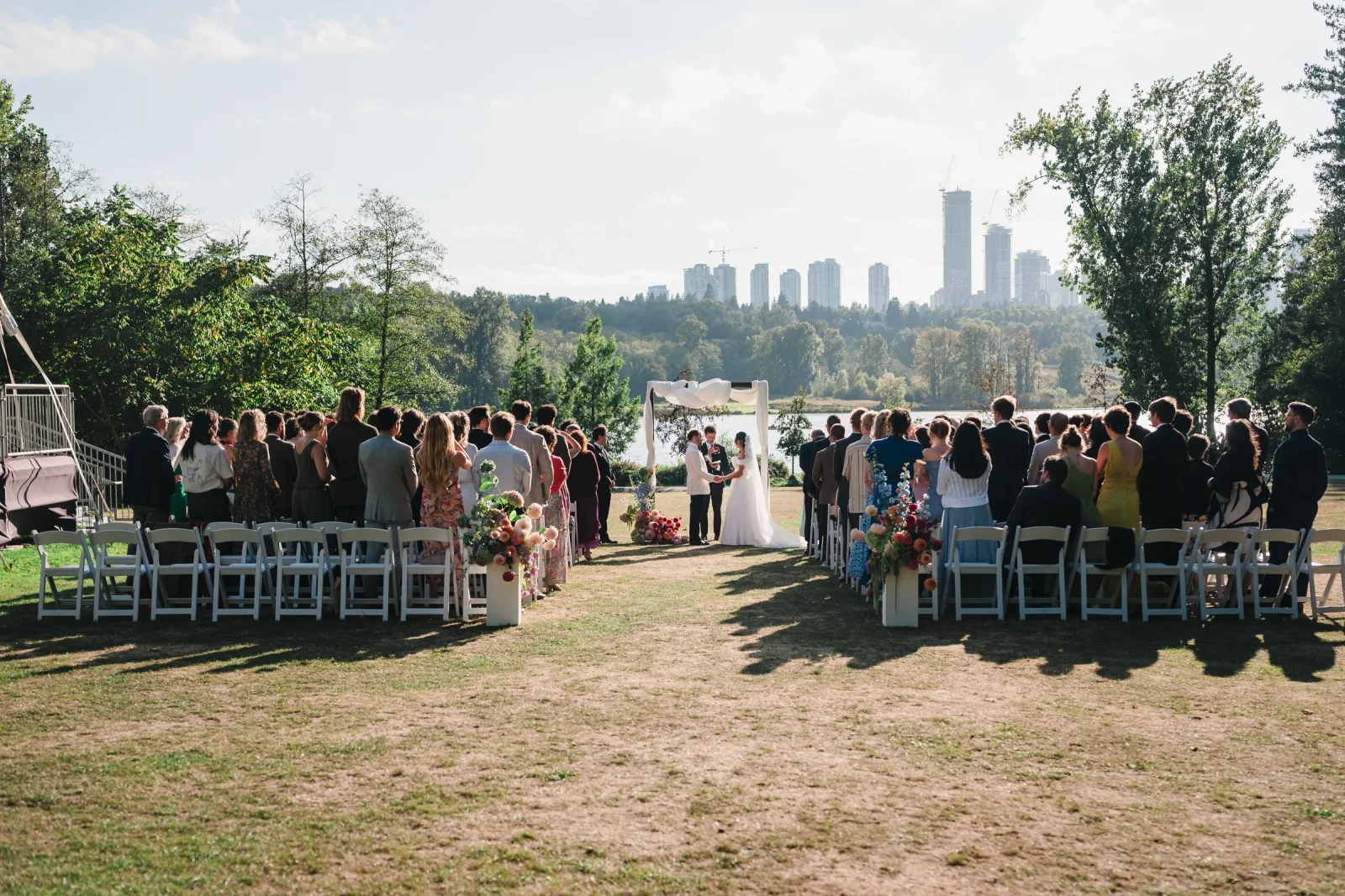 Guests seated facing the arch during the ceremony at Hart House, Burnaby, with city towers behind