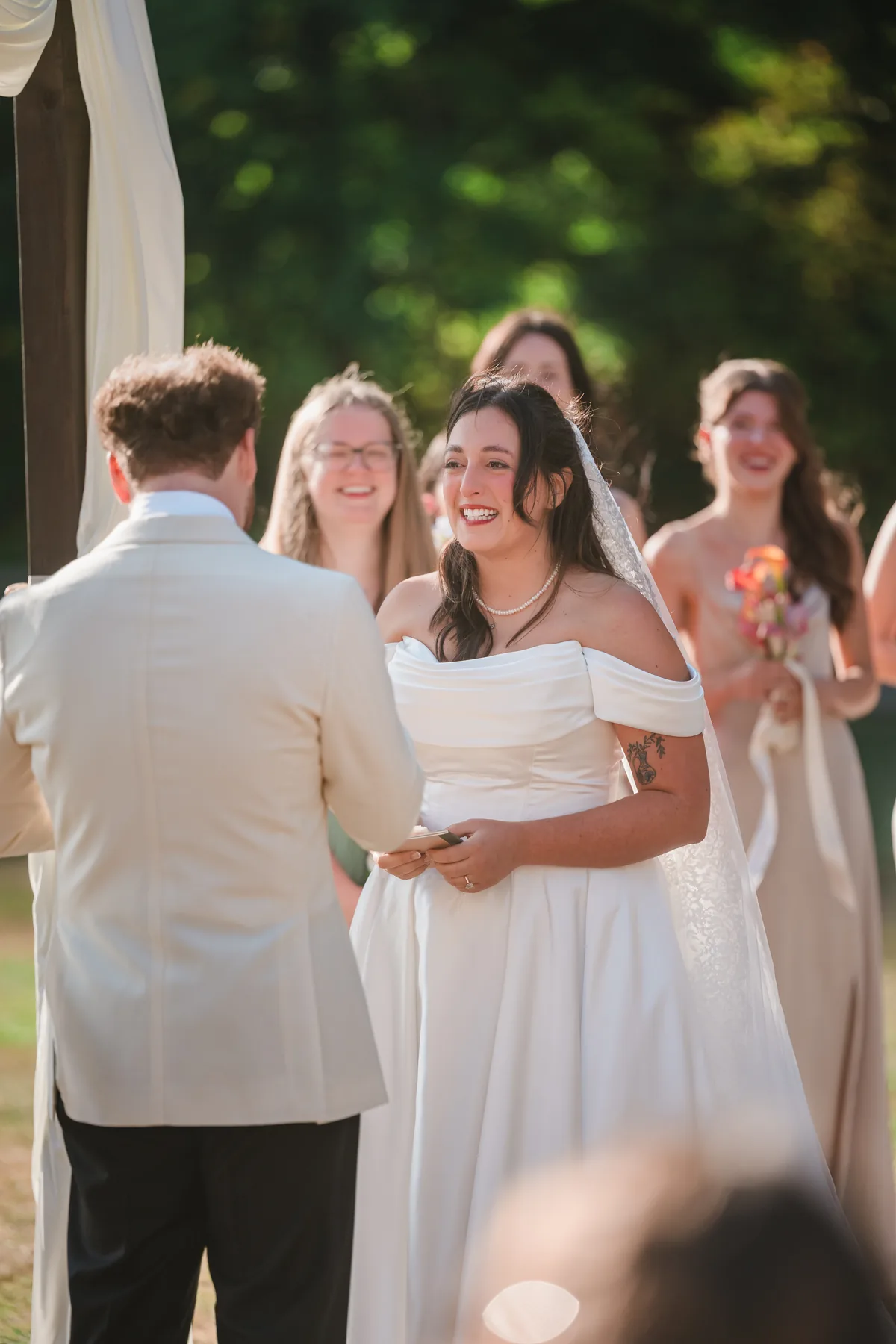Bride laughs while bridesmaids in sage and blush gowns smile behind her