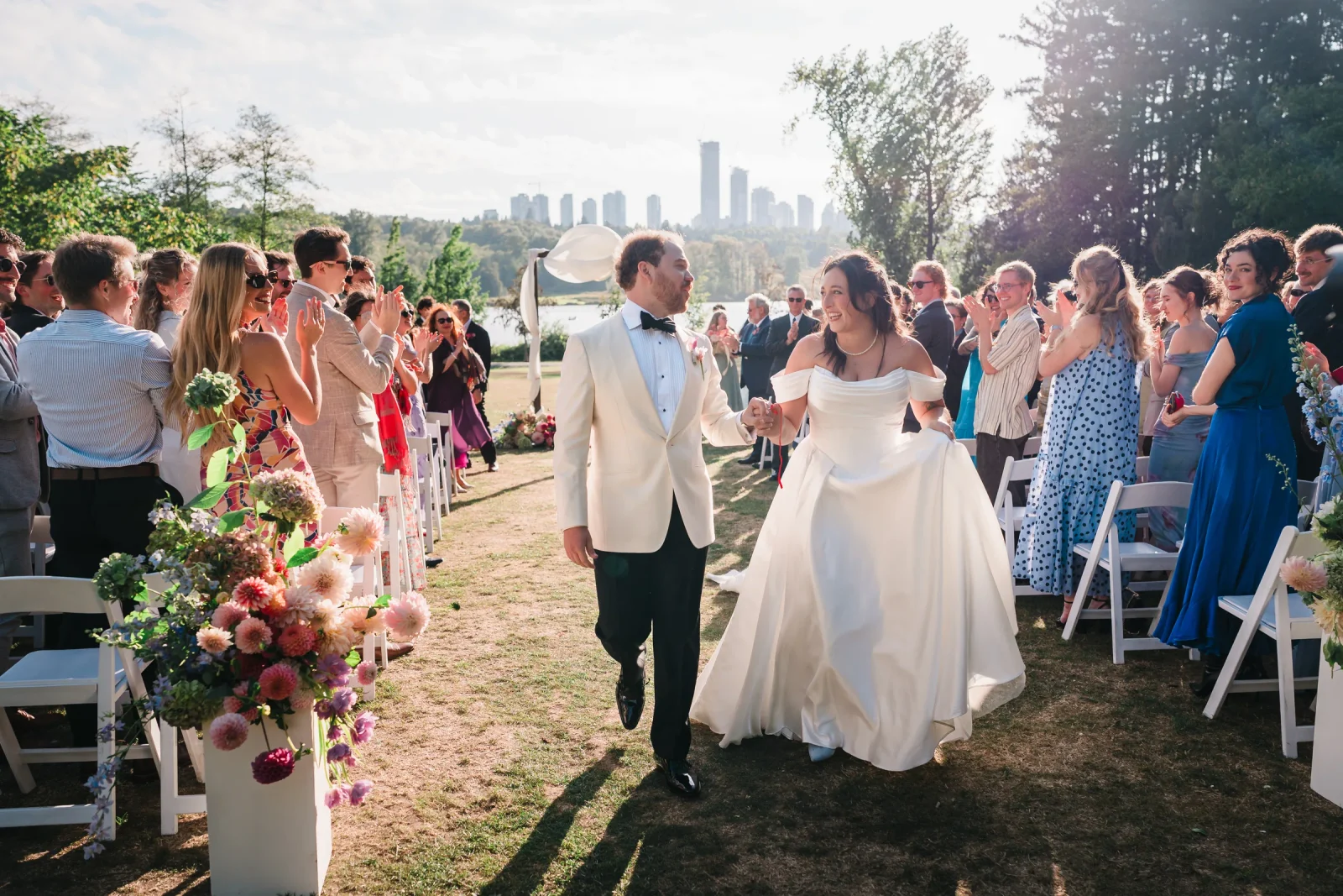 Couple walking hand in hand up the aisle as guests cheer at Hart House, Burnaby