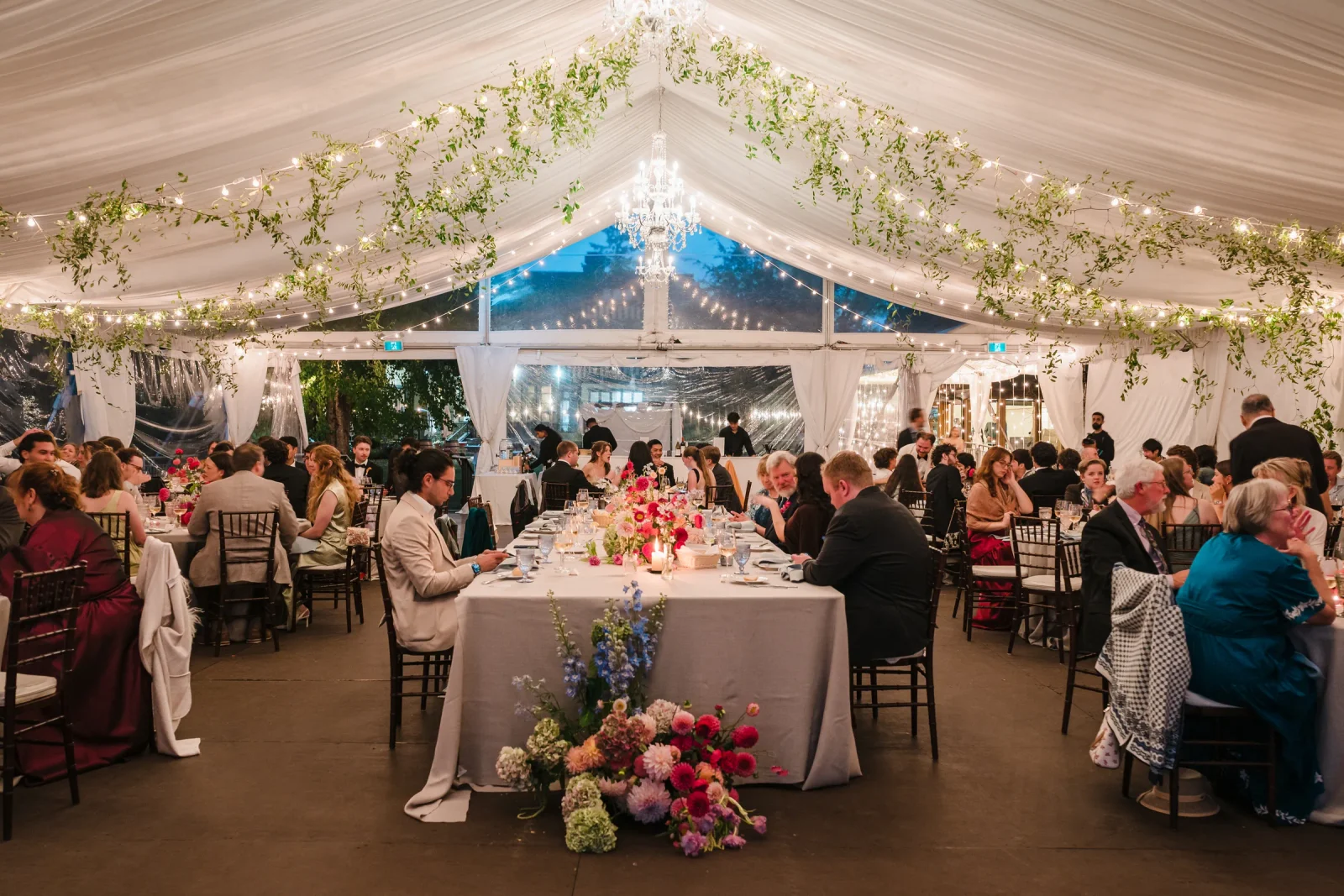 Long candlelit reception table with pink florals and guests seated in a string-lit tent