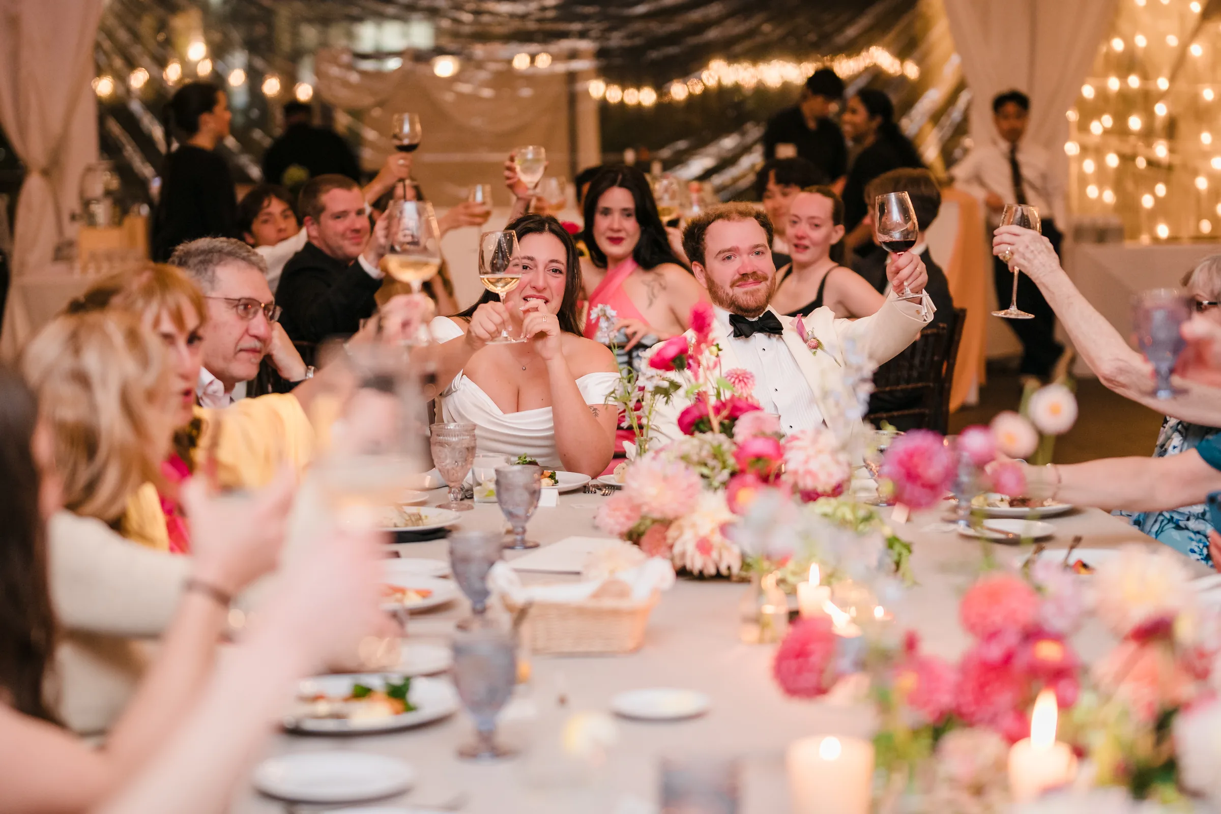 Guests raising glasses around a candlelit reception table with the couple seated at the center