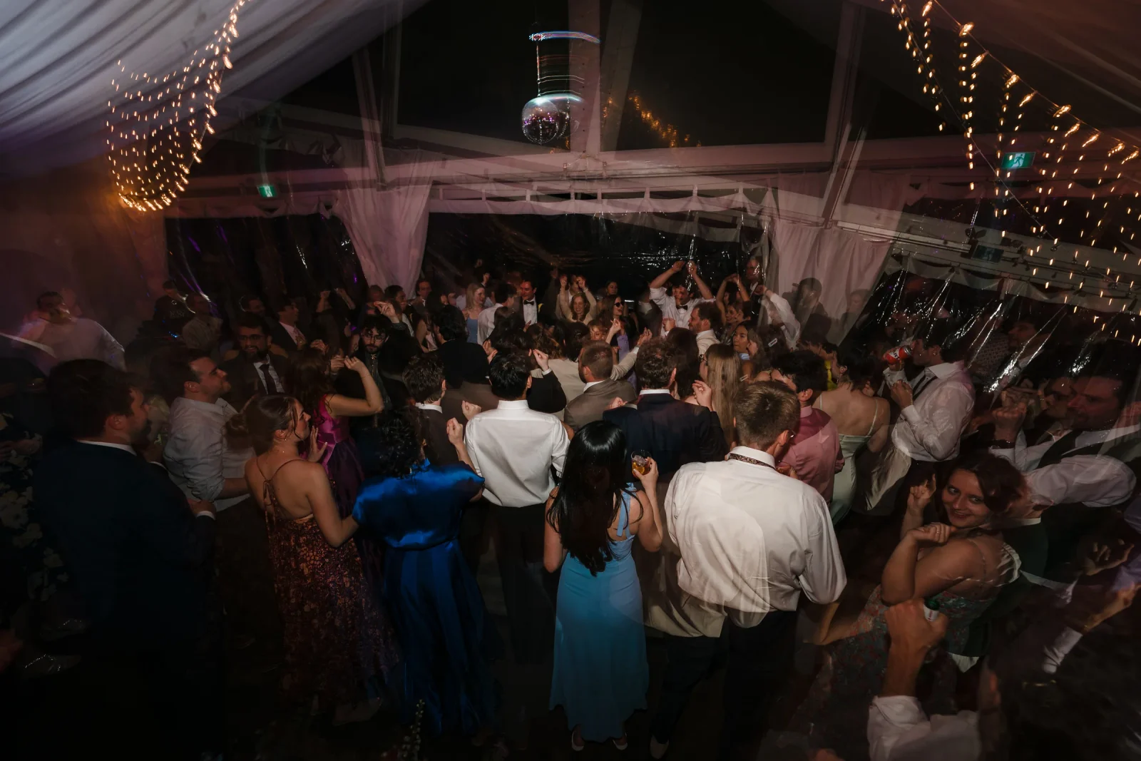 Crowded dance floor of guests under a disco ball and string lights